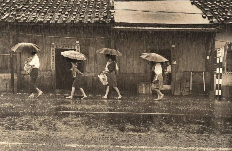 圖3：一群人穿越雨幕。走在前端的男士抱著神明，後面跟著女士背著小朋友。