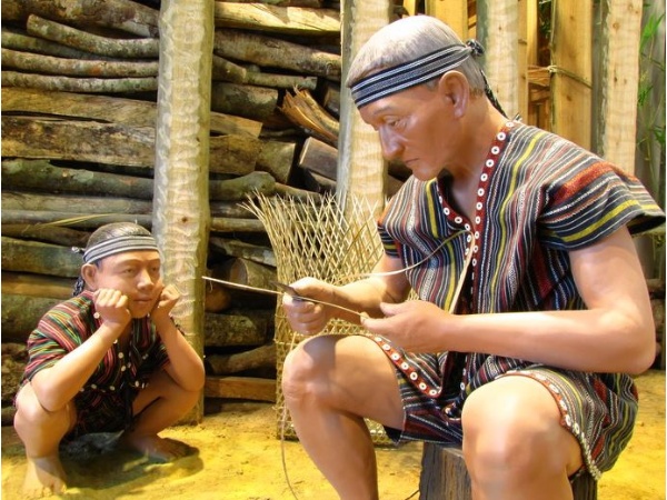 泰雅老人正用小刀修整藤條準備編織藤籃，一旁的小孩默默注視著老人的動作，專注神情也蘊含了傳統文化已在生活中漸漸地傳承下去