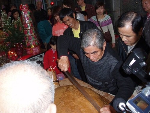 阿發伯持長刀分神龜肉，滿是喜悅地，把精心製作拜過土地公的花生糖龜剖開，分贈給所有在場民眾，同沾土地公的福氣