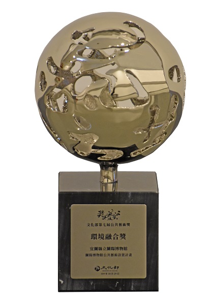 第七屆公共藝術獎獎座由當代書法家董陽孜題字、名藝術家簡俊良設計講座，以不鏽鋼的「天圓」為主調，創見了公共藝術心任天造的特殊精神，更以黑色紋石的「地方」為獎座形式，實踐了藝術與環境空間相輔相成的整合佈局。資料來源：文化部公共藝術獎網站