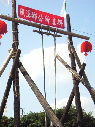 圖2：鞦韆架是用大杉木（韆柱）、桂竹（盪架、握桿）以藤條綑繫架設。頂部3個藤條韆環套住大軸木、小軸木及青桂竹折掛的握桿，中間白繩為安全帶（102.9.28）