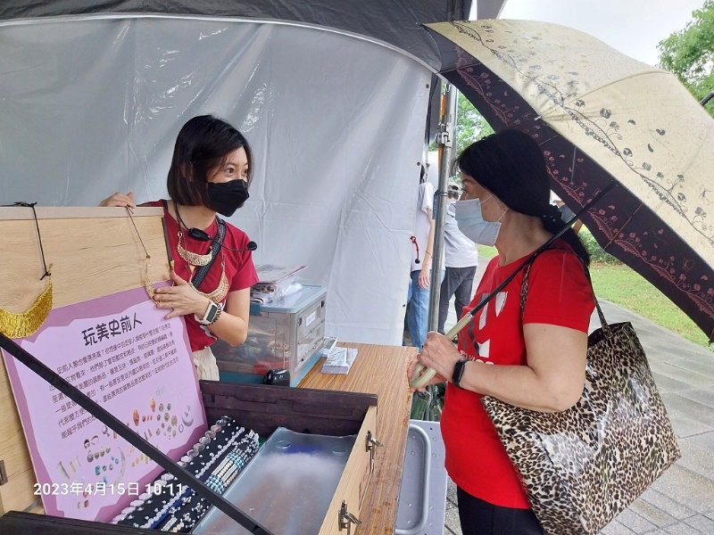 同仁於現場攤位為遊客介紹教具箱內的仿製飾品