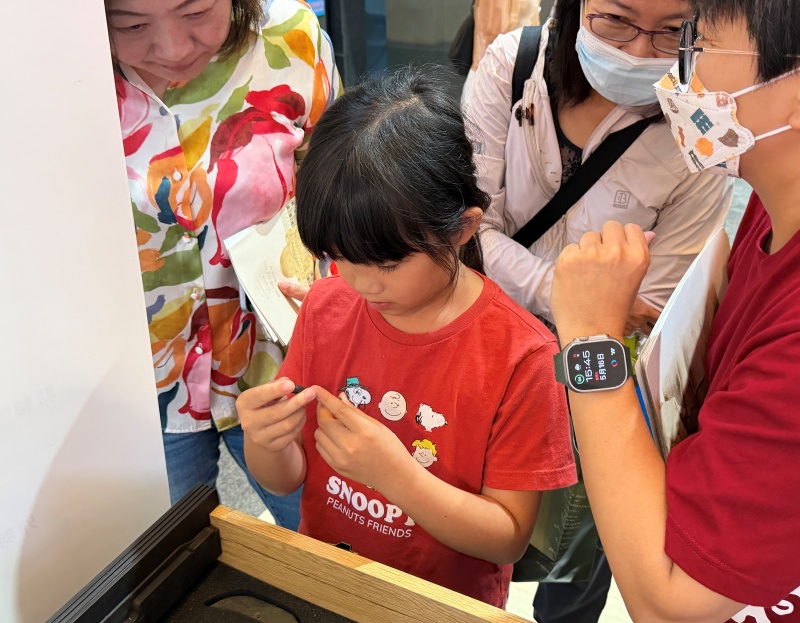 蘭博館的考古教具箱，適合各年齡層及不同需求的民眾體驗，孩童正仔細觀察手上的考古仿品，一旁的大人也跟著細細觀看著。