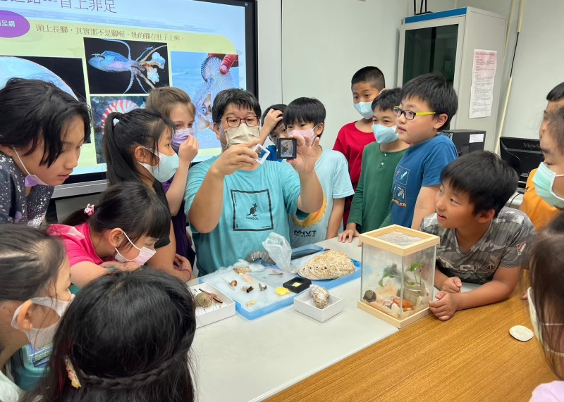 一群學生圍著老師專注地看著老師手上的兩件貝類標本