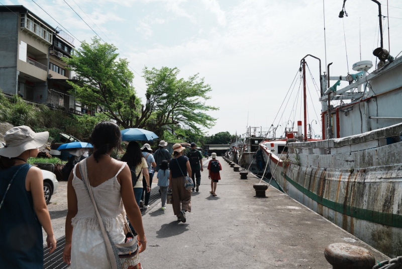 人群經過大溪漁港，漁船停靠於碼頭旁。